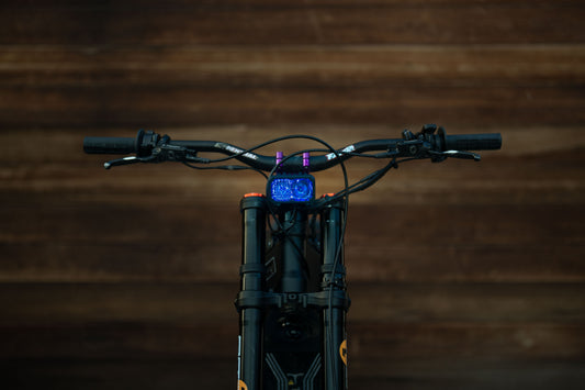 Warp 9 V2 high-output LED headlight mounted on a Surron electric dirt bike — front cockpit view with headlight illuminated