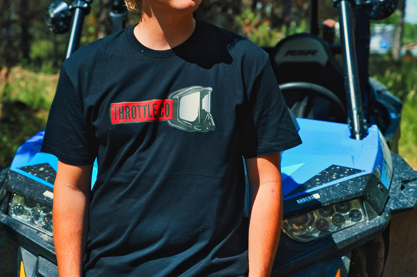 Close-up of the Throttle Co Red Goggles chest graphic on a rider leaning against a blue UTV