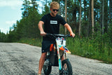 Rider wearing the Throttle Bros Logo Topo Tee standing over a dirt bike on a forest road