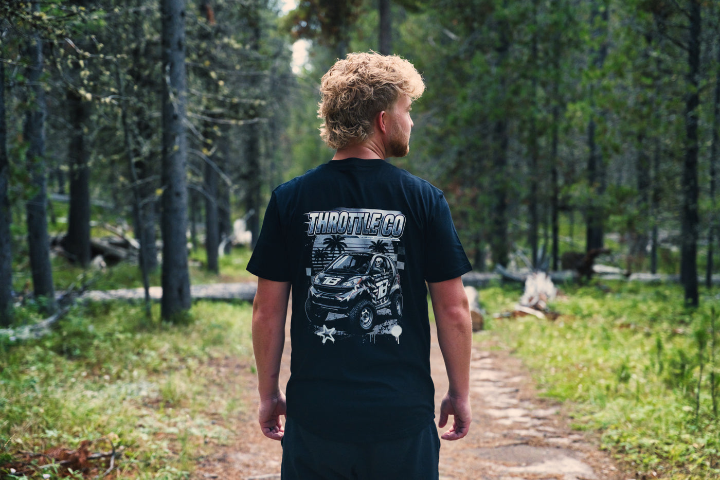 Rider walking away down a forest trail in the Smart Car Throttle Bros Tee, back graphic visible