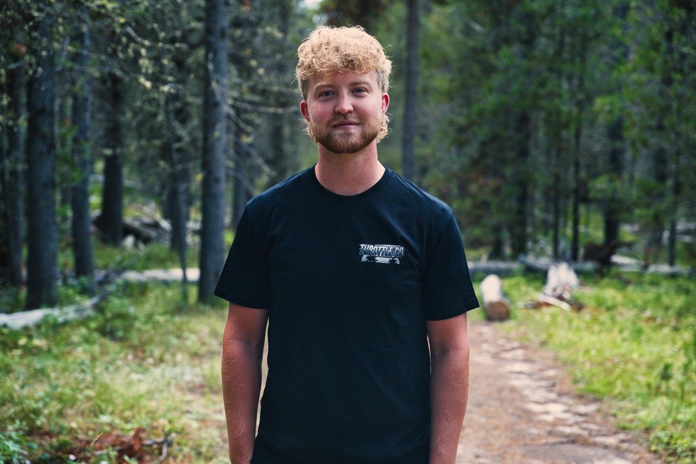 Rider facing the camera on a forest trail wearing the Smart Car Throttle Bros Tee