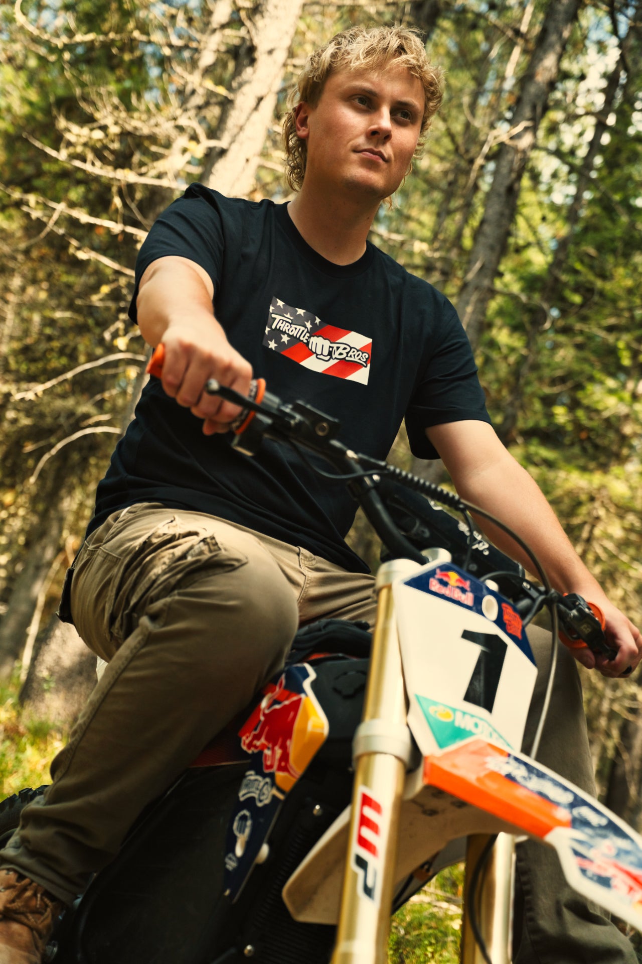Rider wearing the Throttle Bros Logo American Flag Tee seated on a dirt bike in the woods
