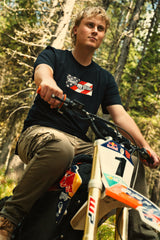 Rider wearing the Throttle Bros Logo American Flag Tee seated on a dirt bike in the woods