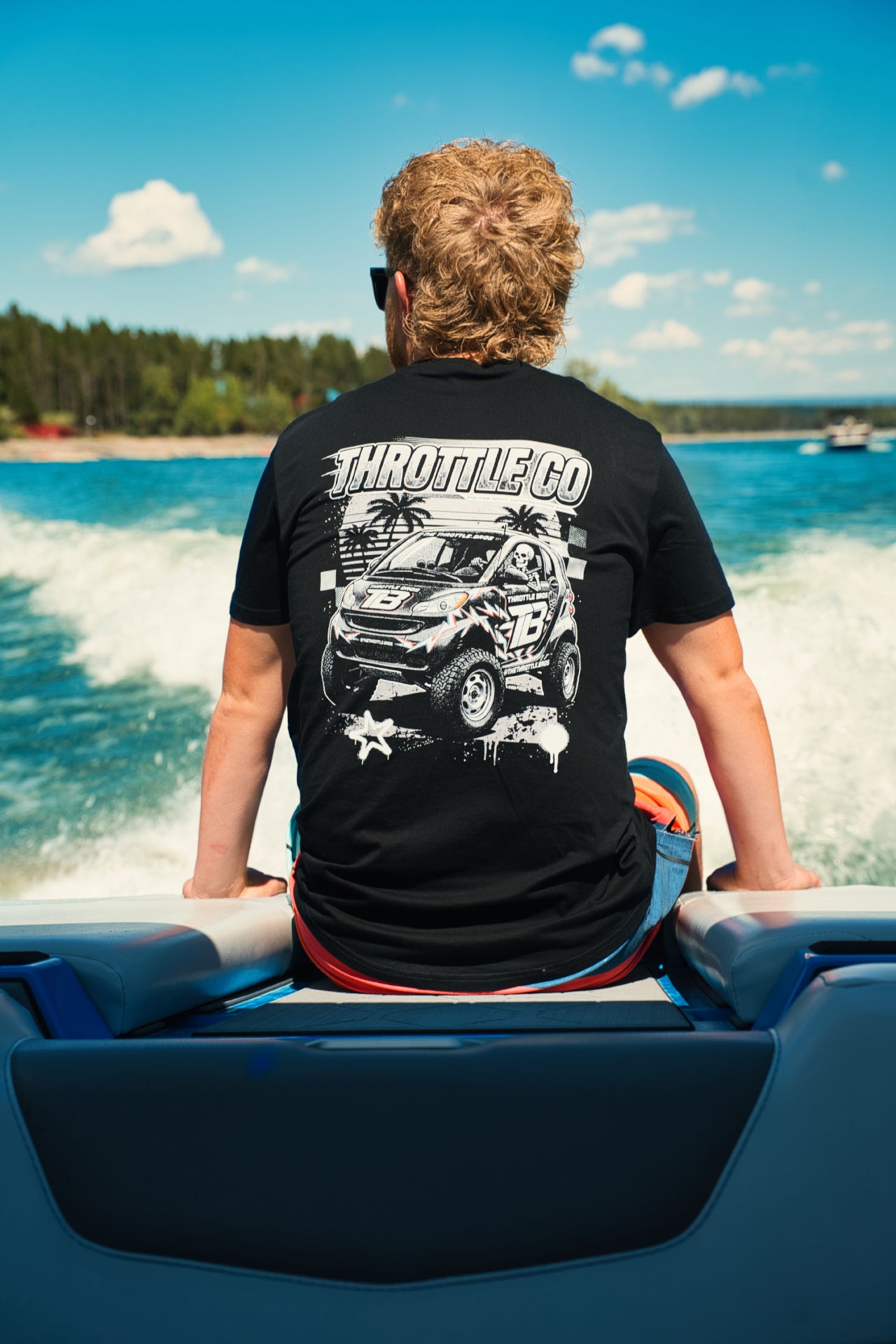 Rider seated on the back of a wake boat wearing the Smart Car Throttle Bros Tee, full back graphic visible