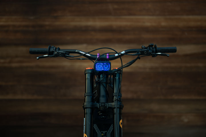 Warp 9 V2 high-output LED headlight mounted on a Surron electric dirt bike — front cockpit view with headlight illuminated
